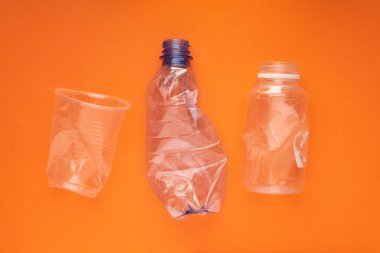 Plastik şişeler ve turuncu arka planda bir fincan çöktü. Plastik kullanım konsepti. Ekolojik sorun, küresel çevre.