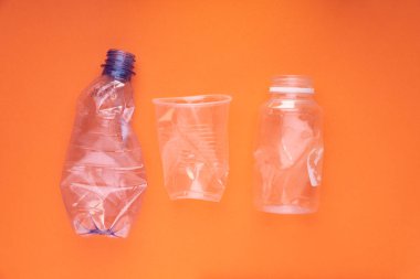 Plastik şişeler ve turuncu arka planda bir fincan çöktü. Plastik kullanım konsepti. Ekolojik sorun, küresel çevre.