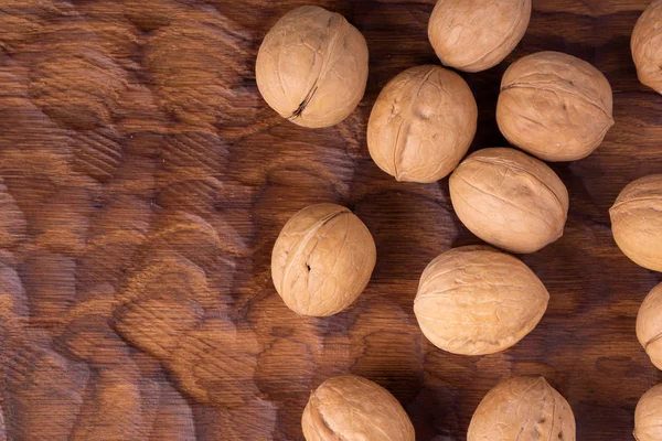 Bunch of whole walnuts lying on carved wooden board. Healthy nuts and seeds composition, background. — Stock Photo, Image