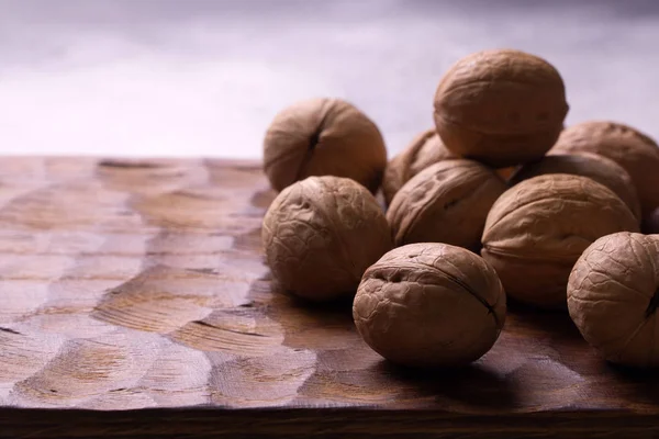 Manojo de nueces enteras tumbadas sobre tabla de madera tallada. Composición saludable de frutos secos y semillas, fondo . —  Fotos de Stock