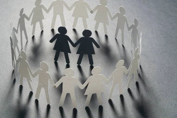 Paper figure of female couple surrounded by circle of paper people holding hands on yellow surface. Bulling, minorities, conflict concept. — Stock Photo, Image
