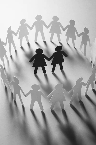 Paper figure of female couple surrounded by circle of paper people holding hands on white surface. Bulling, minorities, conflict concept. — Stock Photo, Image