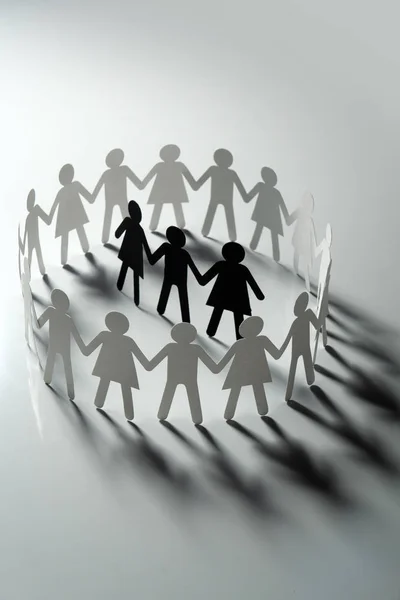 Três figuras de papel humano cercadas por um círculo de pessoas de papel de mãos dadas na superfície branca. Bulling, segregação, conceito de conflito . — Fotografia de Stock