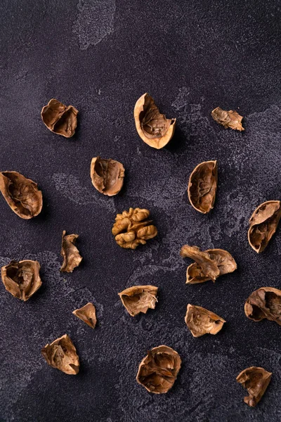 Cáscara de nuez agrietada esparcida por la mesa de pizarra oscura. Composición saludable de frutos secos y semillas . — Foto de Stock