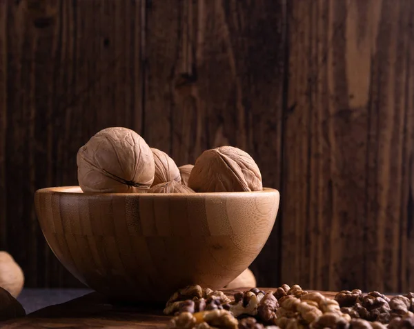 Walnuts in wooden bowl on wooden carved board. Healthy nuts and seeds composition. — Stock Photo, Image