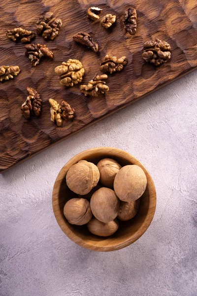 Walnuts in wooden bowl and on wooden carved board on bright textured surface. Healthy nuts and seeds composition. — Stock Photo, Image