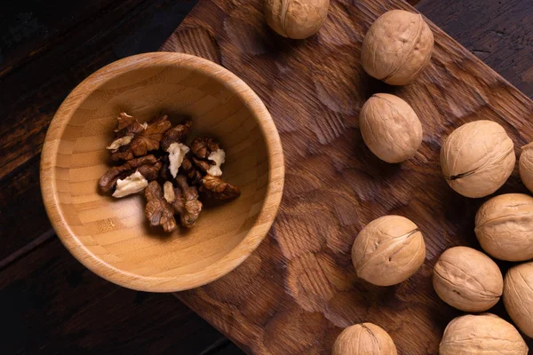 Nueces en cuenco de madera sobre tabla tallada en madera. Composición saludable de frutos secos y semillas . — Foto de Stock