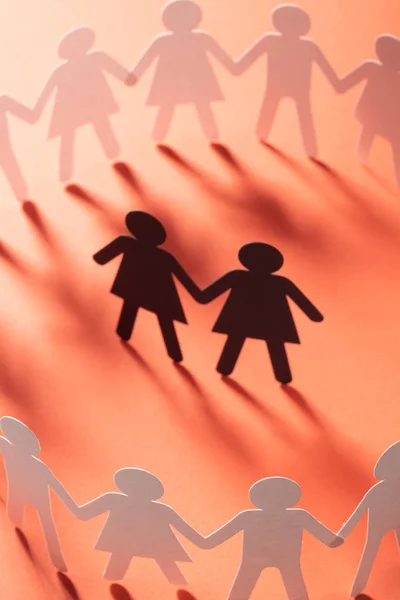 Figurine en papier de couple féminin entouré d'un cercle de gens en papier tenant la main sur la surface rouge. Bulling, minorités, concept de conflit . — Photo