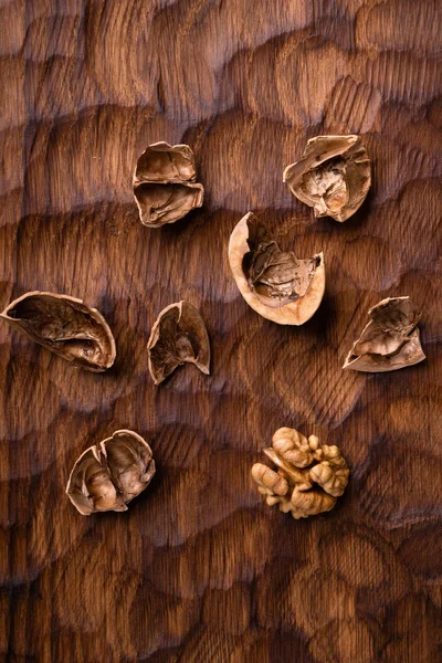 ひび割れたクルミの殻とカーネルは、彫刻された木製のボード全体に散らばっていました。健康的なナッツと種子組成物. — ストック写真