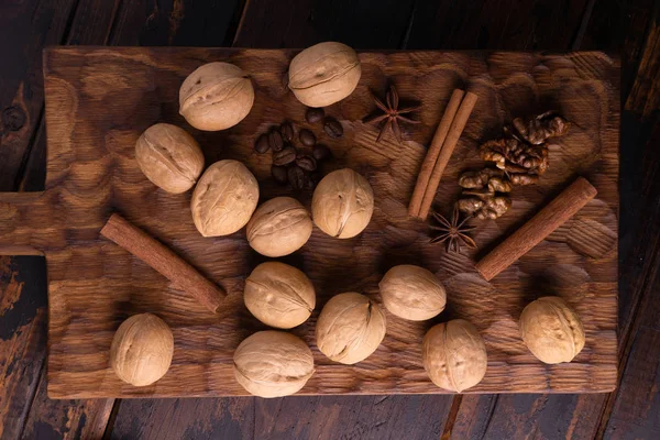 Nueces, canela, anís estrellado y granos de café en una tabla de cortar de madera. Nueces y especias sobre la mesa. Composición de los alimentos, vista superior . —  Fotos de Stock
