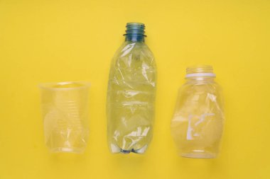 Çökmüş plastik şişeler ve sarı arka planda bir fincan. Plastik kullanım konsepti. Ekolojik sorun, küresel çevre.