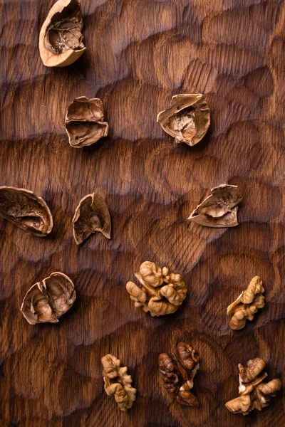 Cáscara de nuez agrietada y granos dispersos a través de la tabla de madera tallada. Composición saludable de frutos secos y semillas . — Foto de Stock
