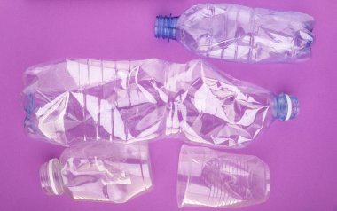 Çökmüş plastik şişeler ve mor arka plan üzerinde bir fincan. Plastik kullanım konsepti. Ekolojik sorun, küresel çevre.