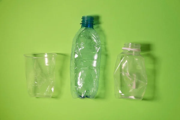 Crashed plastic bottles and a cup on bright green background. Plastic utilisation concept. Ecological problem, global environment. — Stock Photo, Image