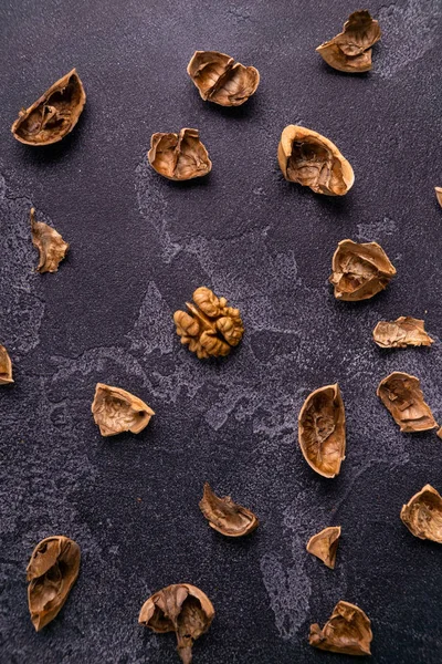 Cáscara de nuez agrietada esparcida por la mesa de pizarra oscura. Composición saludable de frutos secos y semillas . — Foto de Stock