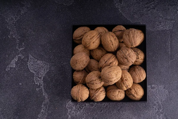 Nueces enteras y agrietadas en una placa cuadrada sobre una superficie de textura azul, vista superior. Composición saludable de frutos secos y semillas . —  Fotos de Stock