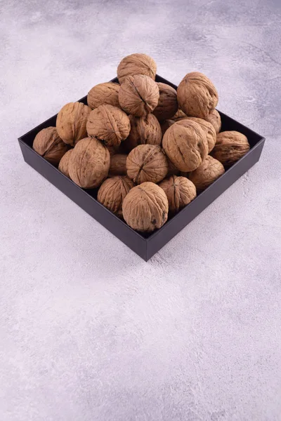 Walnuts on a square plate on bright textured surface, side view. Healthy nuts and seeds composition. — Stock Photo, Image