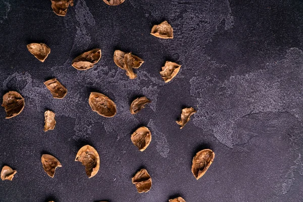 Cáscara de nuez agrietada esparcida por la mesa de pizarra oscura. Composición saludable de frutos secos y semillas . — Foto de Stock