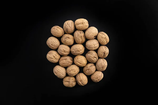 Walnuts in shell in the center on black surface, top view. Background of round walnuts. Healthy nuts and seeds composition. — Stock Photo, Image