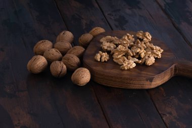 Kesme tahtası ve ahşap siyah masa üzerinde kırık ve bütün ceviz, yan görünüm. Sağlıklı fındık ve tohum bileşimi.