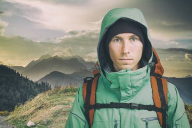 Bulutlu arka planda genç bir erkek yürüyüşçü kameraya bakıyor. Ön manzara. Etkin yaşam tarzı ve turizm.