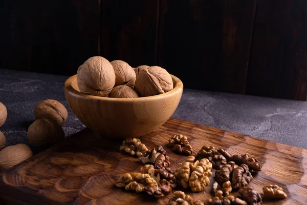 Nueces en cuenco de madera sobre tabla tallada en madera. Composición saludable de frutos secos y semillas . —  Fotos de Stock