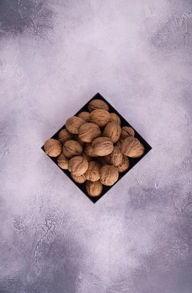 Nueces en una placa cuadrada sobre una superficie de textura brillante, vista superior. Composición saludable de frutos secos y semillas . —  Fotos de Stock