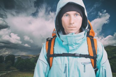 Bulutlu arka planda genç bir erkek yürüyüşçü kameraya bakıyor. Ön manzara. Etkin yaşam tarzı ve turizm.