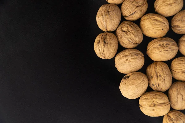 Walnuts in shell on black surface, top view. Background of round walnuts. Healthy nuts and seeds composition. — Stock Photo, Image