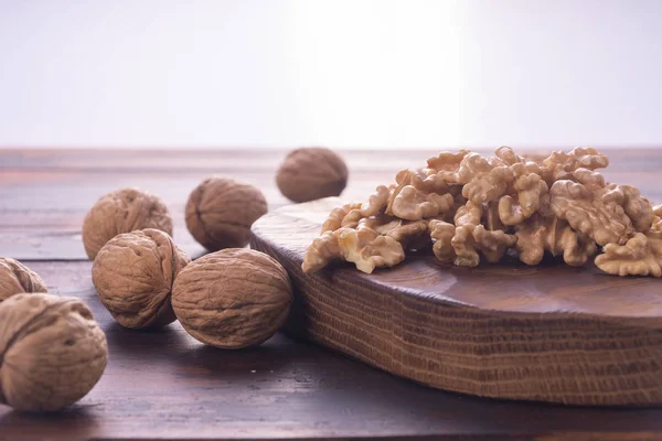 まな板と木製のテーブルにひび割れと全体のクルミ、白い背景に側面のビュー。健康的なナッツと種子組成物. — ストック写真