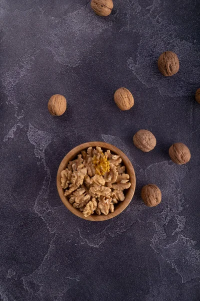 Cracked and whole walnuts in wooden bowl and on dark slate surface. Healthy nuts and seeds composition. — Stock Photo, Image