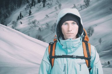 Genç bir dağ tırmanışçısı kışın dağ manzaralı kameraya bakıyor. Ön manzara. Soğuk havada aktif yaşam tarzı.