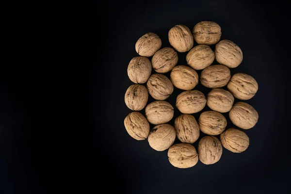 Nueces en cáscara en el centro en la superficie negra, vista superior. Fondo de nueces redondas. Composición saludable de frutos secos y semillas . —  Fotos de Stock
