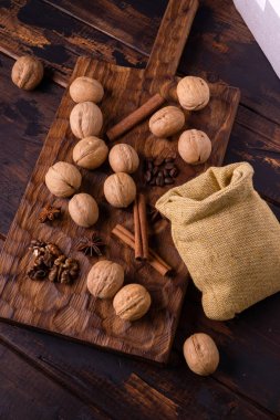 Ceviz, tarçın, yıldız anason, kahve çekirdekleri ve ahşap kesme tahtası üzerinde küçük bir çanta. Masada fındık ve baharatlar var. Gıda bileşimi.