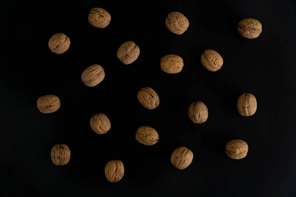 Nueces en la cáscara en la superficie negra, vista superior. Fondo de nueces redondas. Composición saludable de frutos secos y semillas . — Foto de Stock