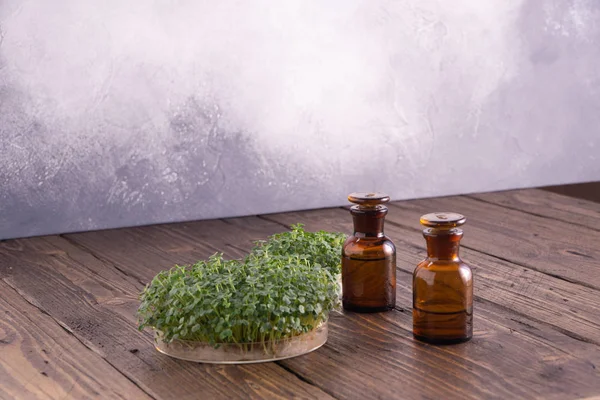 Microgreens in round container and small glass vials on wooden table. Sprouts, microgreens, healthy eating concept. Science, biology.