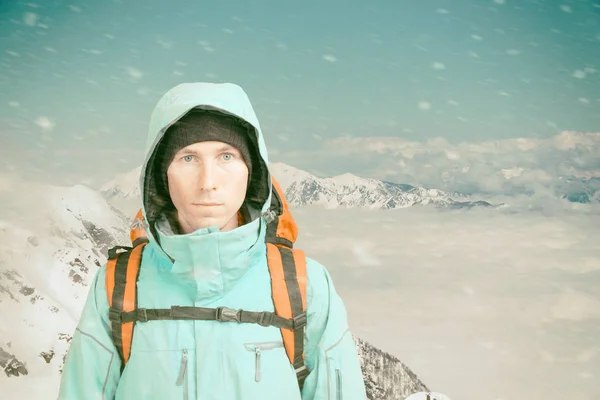 Νεαρός αρσενικός ορειβάτης στη χειμερινή βουνοκορφή κοιτάζοντας την κάμερα. Μπροστά. Ενεργός τρόπος ζωής σε κρύο καιρό. Χειμερινό ορεινό τοπίο και συννεφιά. — Φωτογραφία Αρχείου