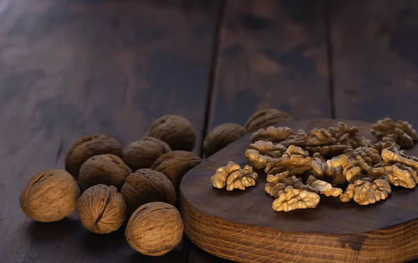 Cracked and whole walnuts on cutting board and wooden table, side view. Healthy nuts and seeds composition. — Stock Photo, Image