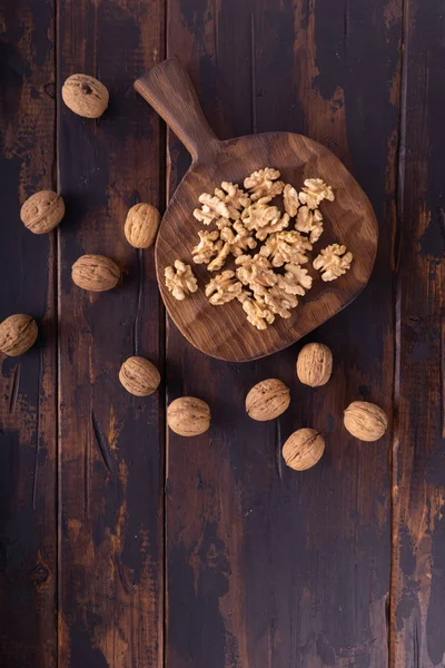 Nueces agrietadas y enteras en tabla de cortar y mesa de madera, vista superior. Composición saludable de frutos secos y semillas . — Foto de Stock