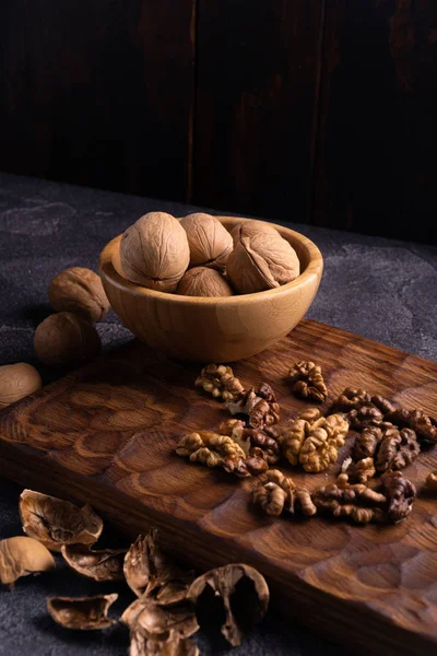 Walnuts in wooden bowl on wooden carved board. Healthy nuts and seeds composition. — Stock Photo, Image