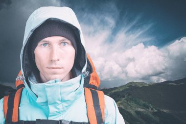 Bulutlu arka planda genç bir erkek yürüyüşçü kameraya bakıyor. Ön manzara. Etkin yaşam tarzı ve turizm.