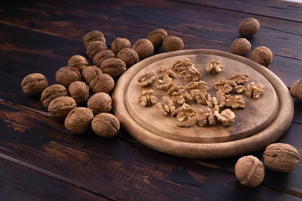 Cracked and whole walnuts on round wooden plate and wooden table, side view. Healthy nuts and seeds composition. — Stock Photo, Image