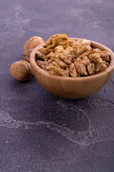 Cracked and whole walnuts in wooden bowl and on dark slate surface. Healthy nuts and seeds composition. — Stock Photo, Image
