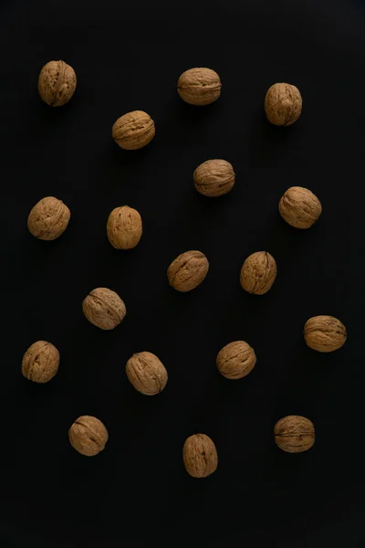 Valnötter i skalet på svart yta, uppifrån. Bakgrund av runda valnötter. Friska nötter och frön sammansättning. — Stockfoto