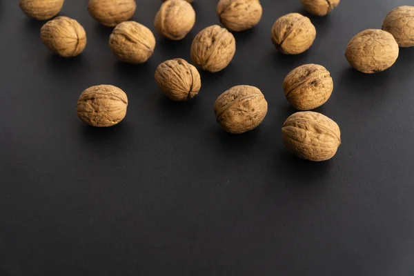 Valnötter i skalet på svart yta, sidovy. Friska nötter och frön bakgrund. — Stockfoto