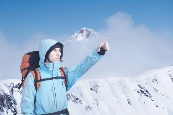 Portrait of adventurous young man on winter mountain top view pointing out. — Stock Photo, Image