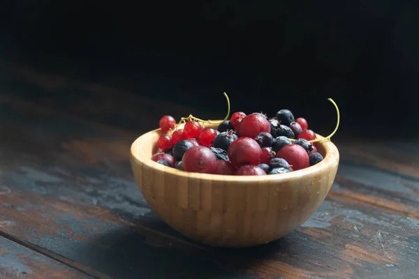 Ripe black and red currants in a wooden bowl on a wooden table. Organic food, berries, harvest season. — Stock Photo, Image