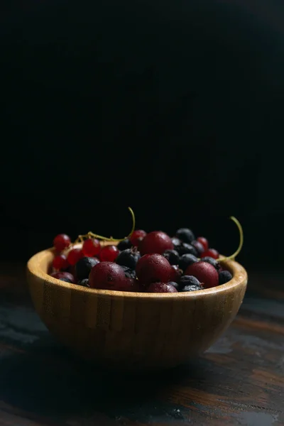 Grosellas maduras negras y rojas en un tazón de madera sobre una mesa de madera. Alimentos orgánicos, bayas, temporada de cosecha . — Foto de Stock