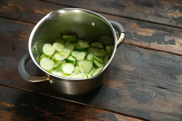 Sliced cucumbers in a pot on rustic wooden table. Top view. — Stock Photo, Image