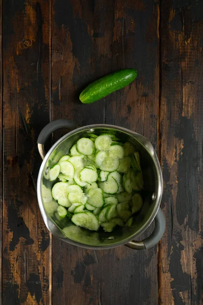 Sliced cucumbers in a pot on rustic wooden table. Top view. — Stock Photo, Image